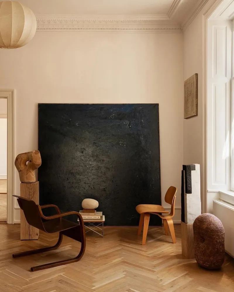 A monolithic black canvas leaning on the wall among wood and marble sculptures, herringbone oak floor